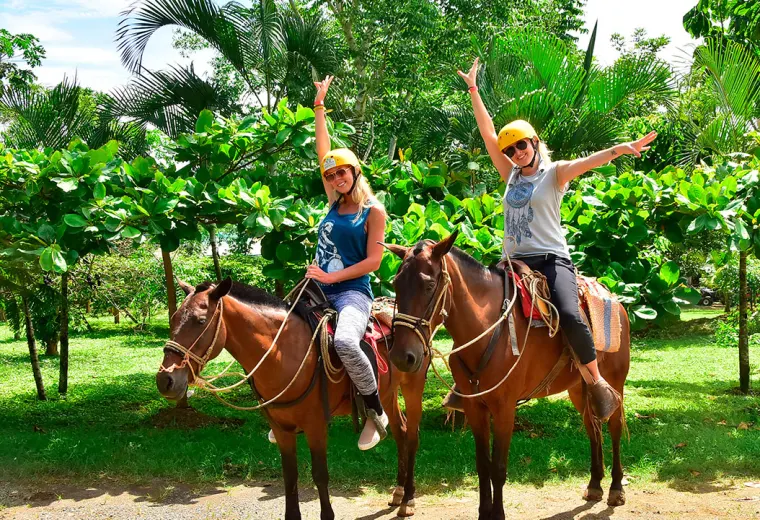 Two riders on horseback among palms, waving